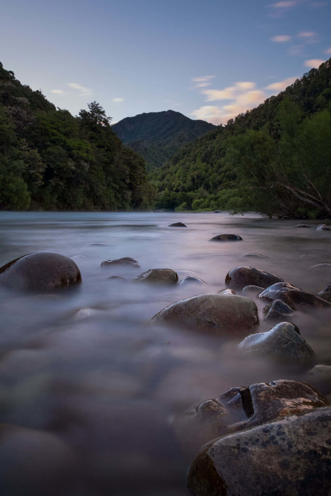 Langzeitbelichtung eines Flusses mit Steinen und Wald im Hintergrund