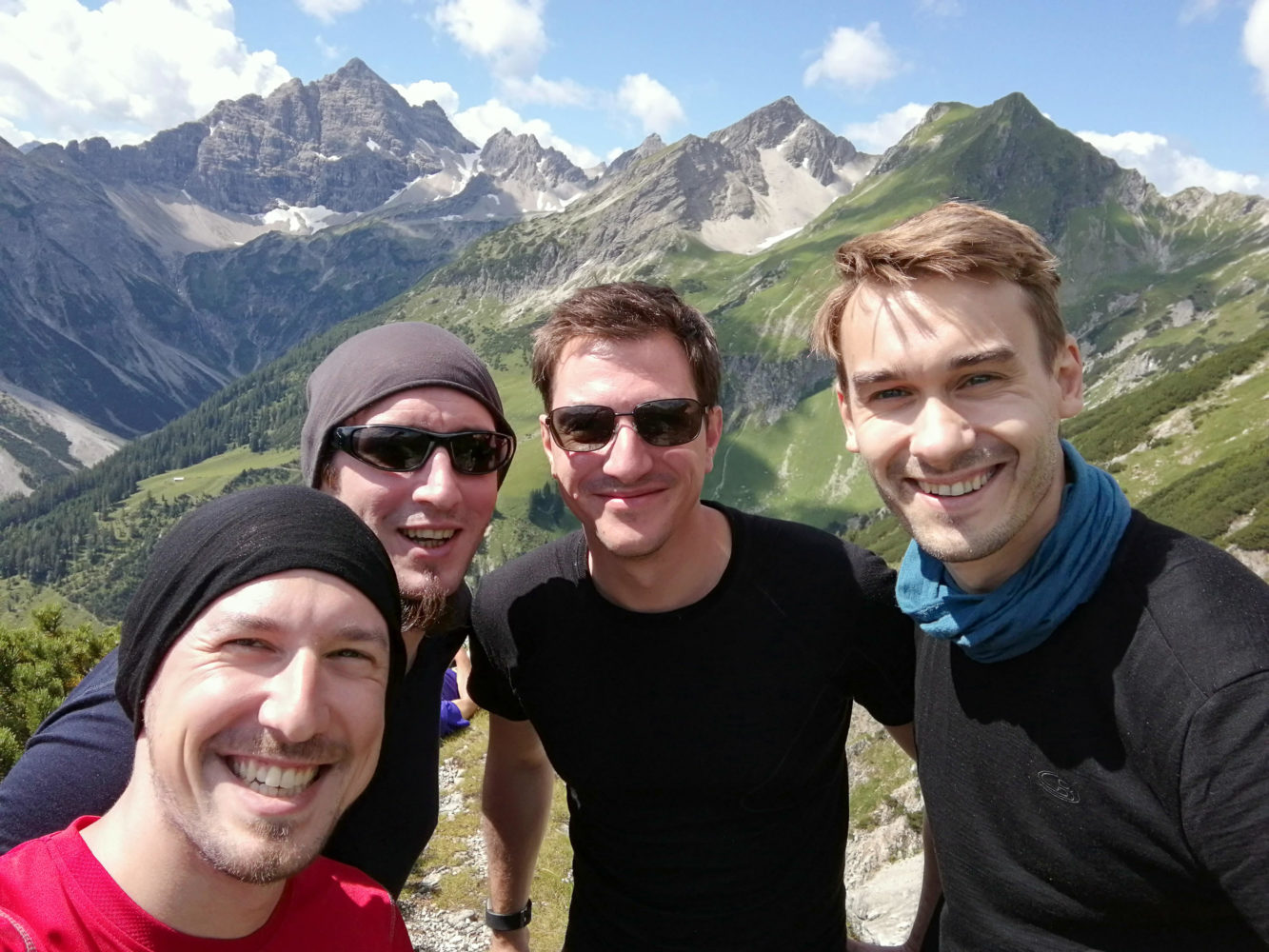 4 Männer blicken vor Bergpanorama in die Handykamera
