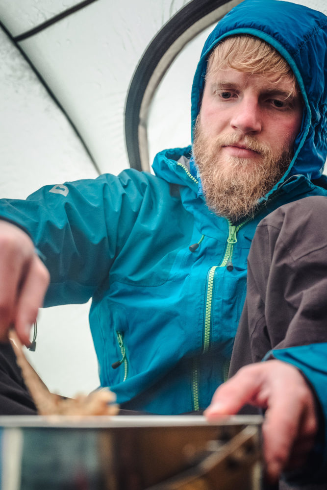 Wanderer sitzt im Zelt und kocht auf einem Gaskocher