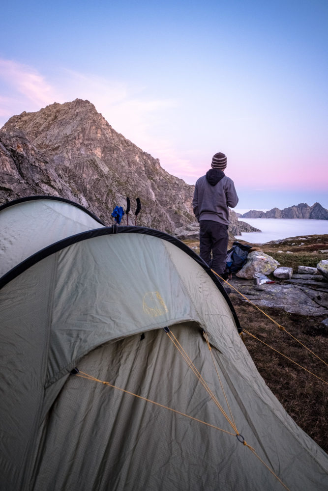 Wanderer steht vor Zelt und blickt auf die Berge