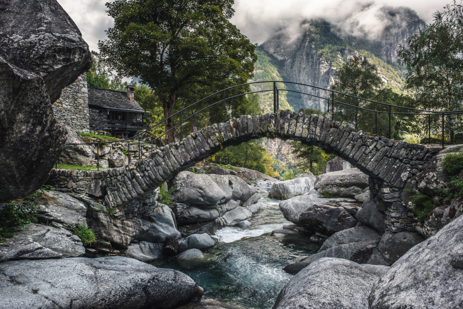 Steinbrücke im Val Bavona über einen Fluss mit Bergen im Hintergrund