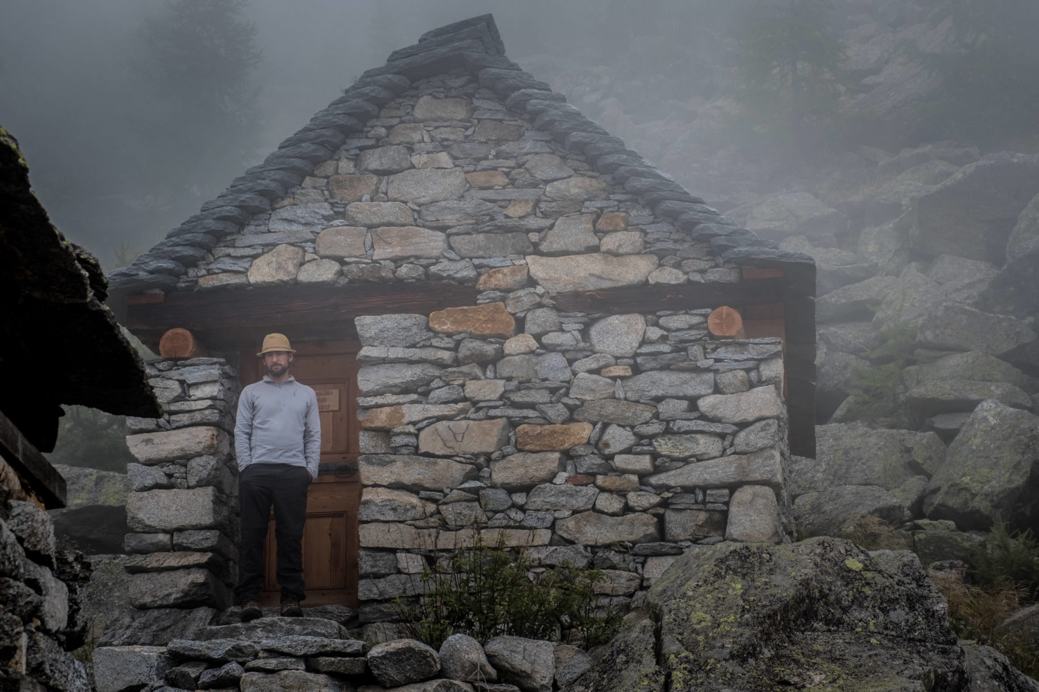 Mann mit Hut steht vor einer Steinhütte