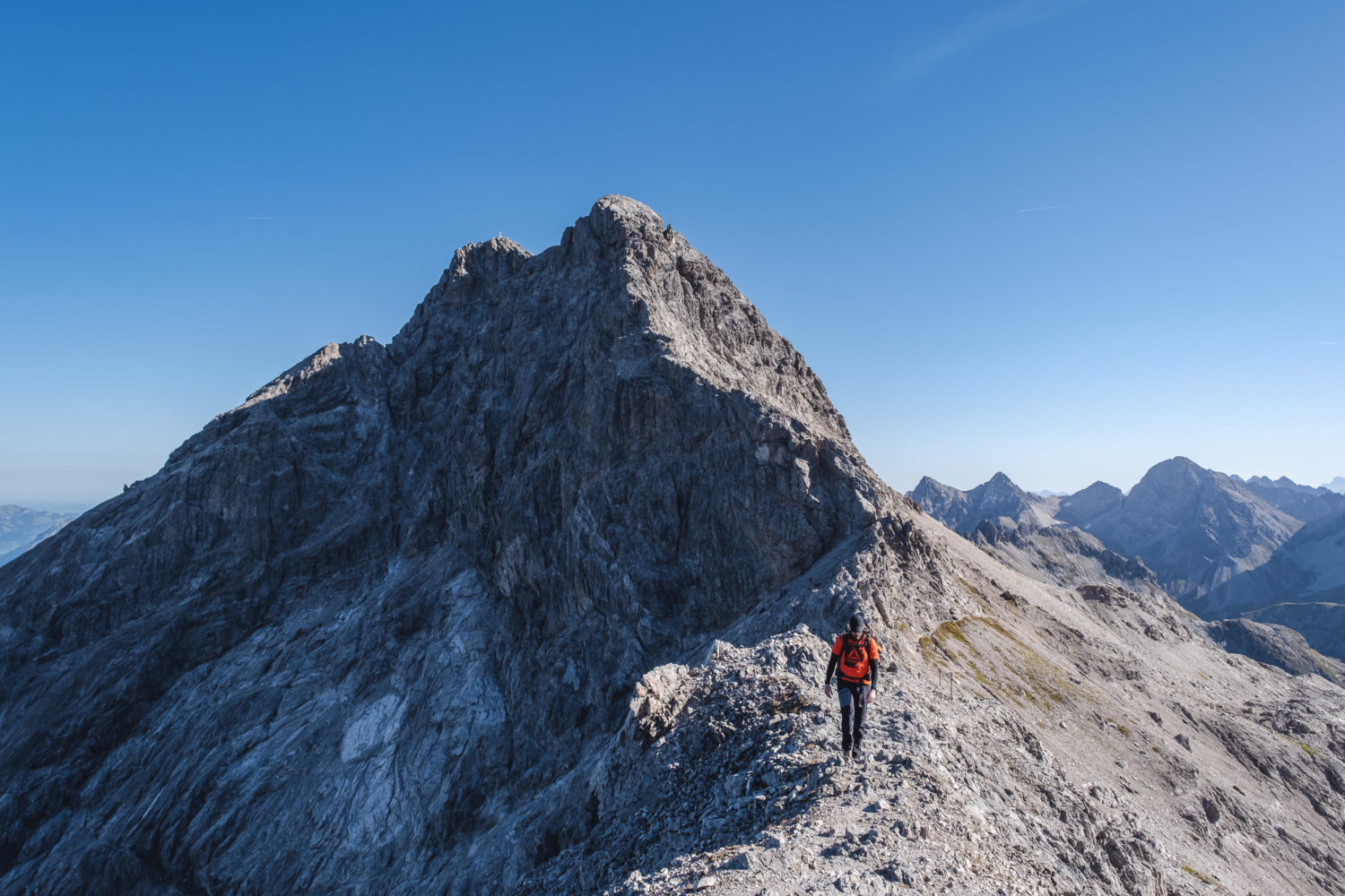Wanderer geht über einen Grat mit Bergspitze im Hintergrund
