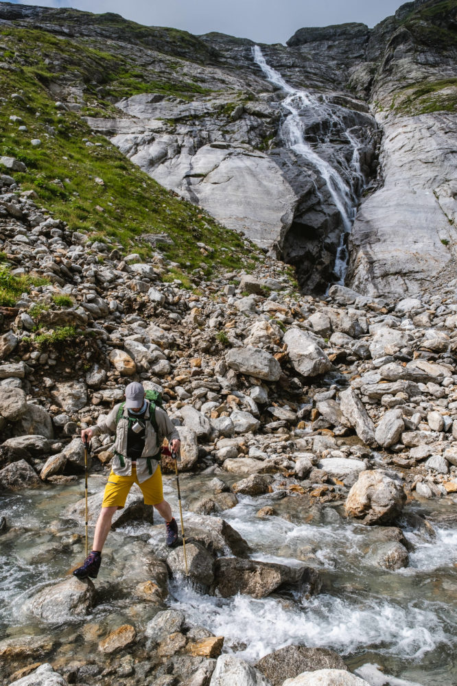 Wanderer geht über einen Fluss mit Wasserfall im Hintergrund
